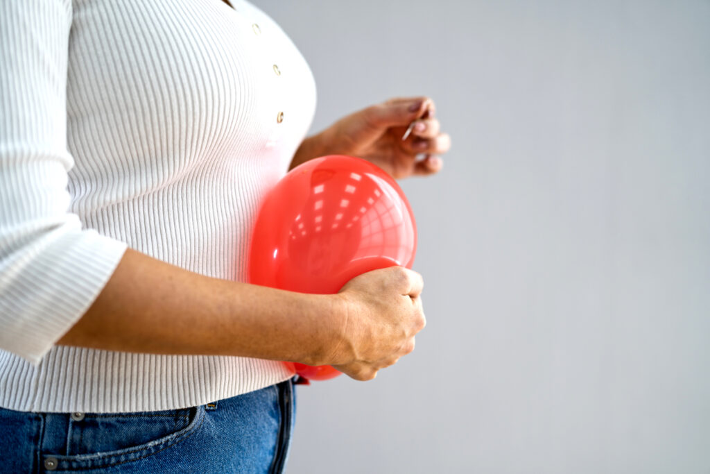 Bloating - lady popping a balloon held next to her stomach