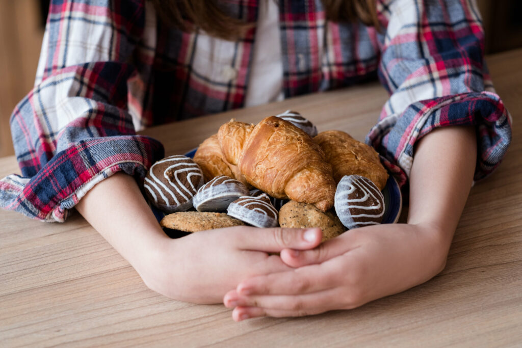 A young girl holding a plate of croissants and pastries.