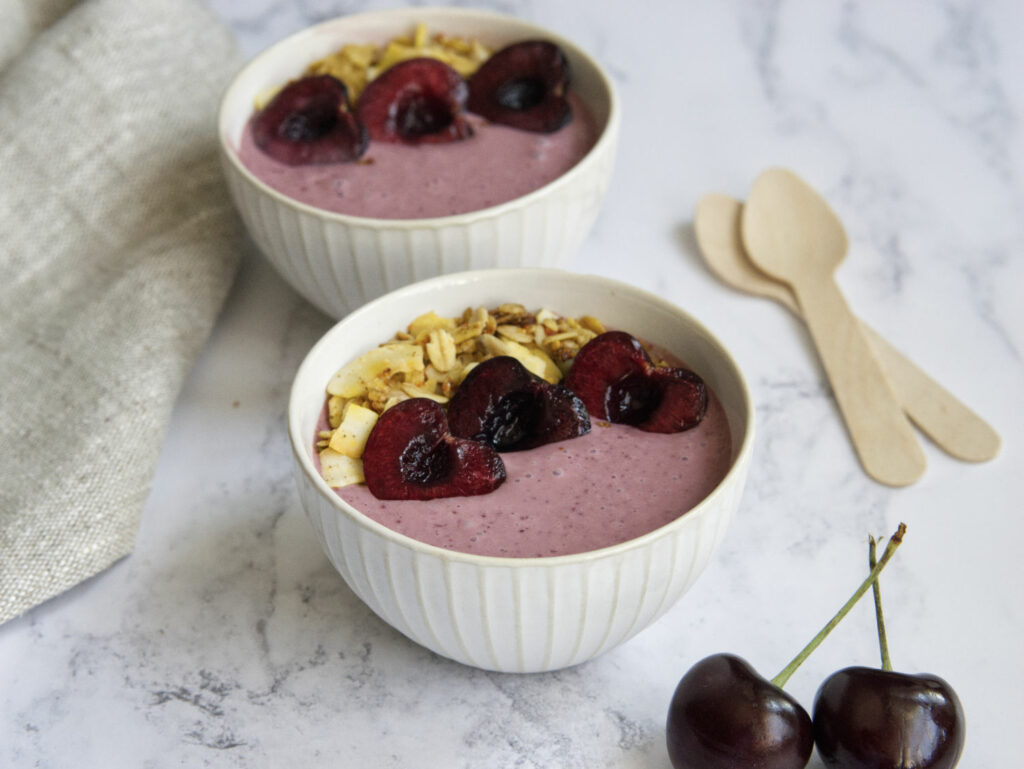 Two bowls with cherries and granola in them.