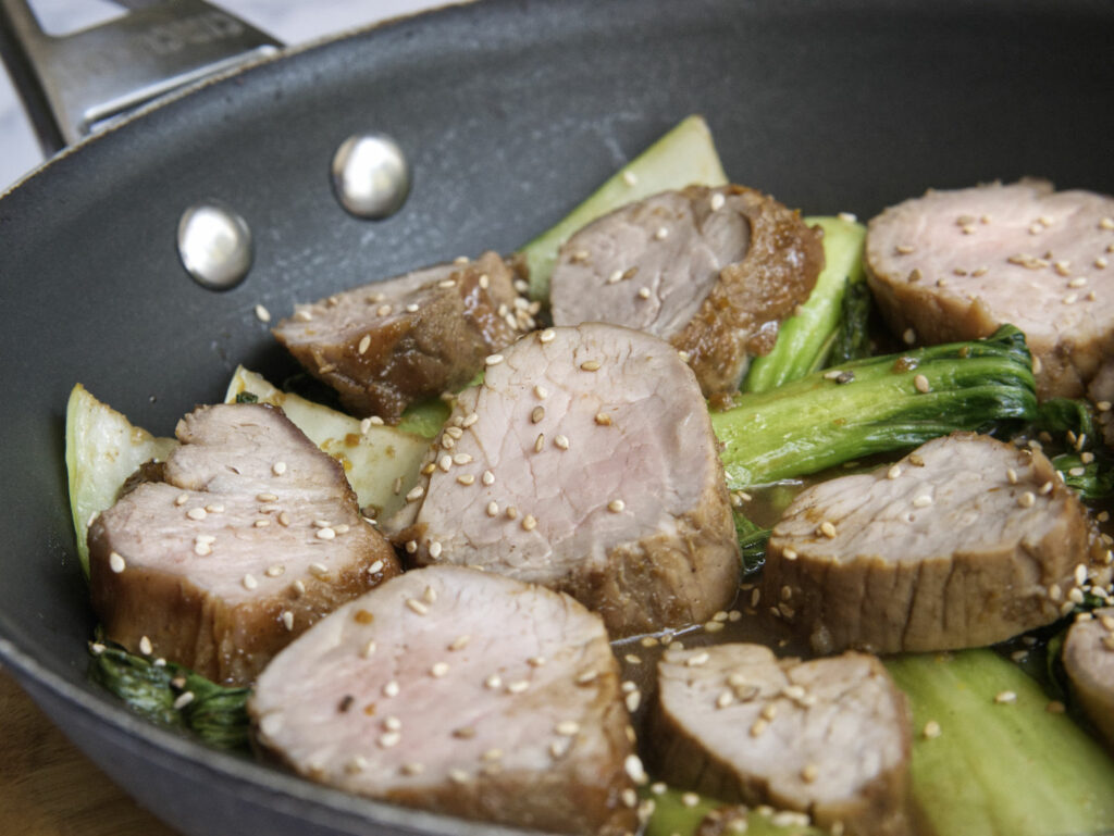 Pork tenderloin in a frying pan with sesame seeds.