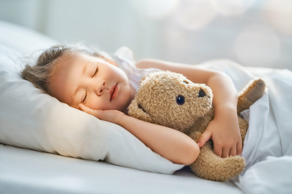 A little girl sleeping in bed with a teddy bear.