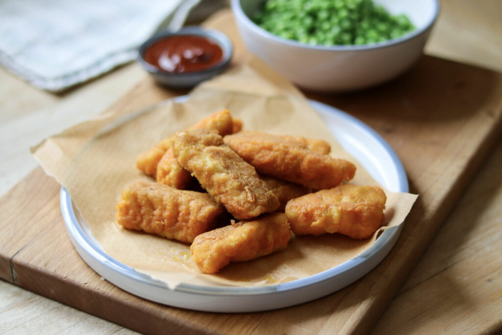 Fish fingers on a plate with ketchup and peas