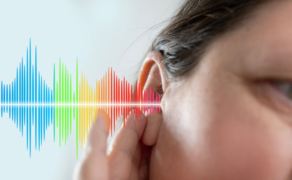 A person touching their ear with a colorful audio wave graphic emanating from it, symbolizing sound or hearing. The waves transition through blue, green, yellow, and red hues, reflecting the range of frequencies.