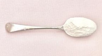 A silver spoon filled with white powder, chickpea flour, resting on a light pink surface.