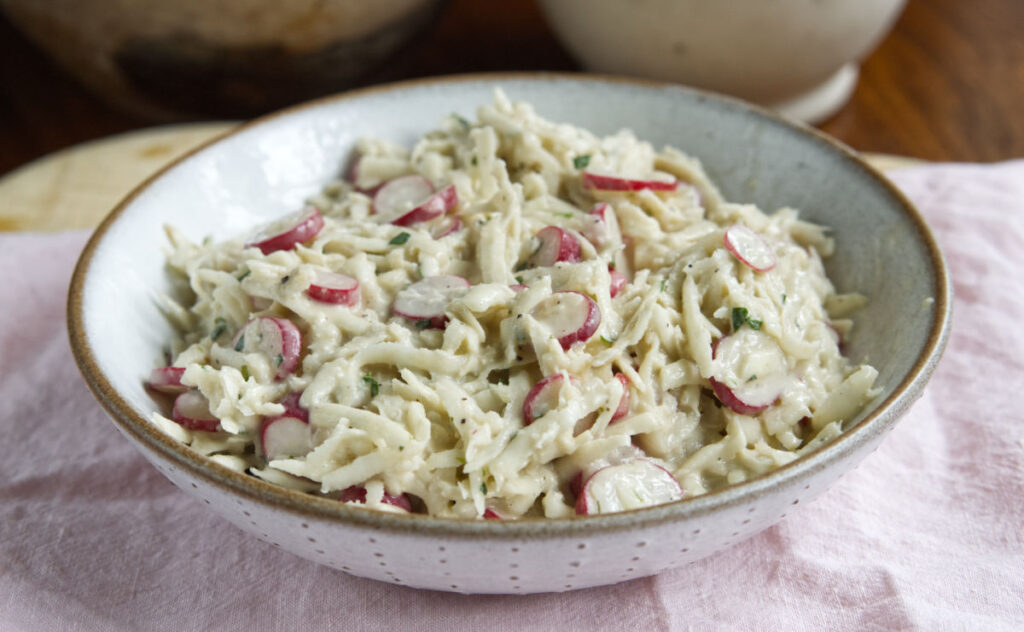 A ceramic bowl filled with Celeriac and Radish Remoulade, placed on a pink cloth.